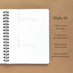 Open spiral-bound softcover reading journal notebook showing review template option Style 2A featuring two book reviews per page and nine review lines plus book details per review with space to attach printed book covers, displayed on a brown background