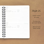 Open spiral-bound softcover reading journal notebook showing review template option Style 2C featuring two book reviews per page and ten review lines plus book details per review, displayed on a brown background