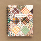 Spiral-bound hardcover reading journal notebook with autumn patchwork cover design on a brown background