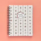 Spiral-bound softcover reading journal notebook with books and bows coquette cover design on a peach background