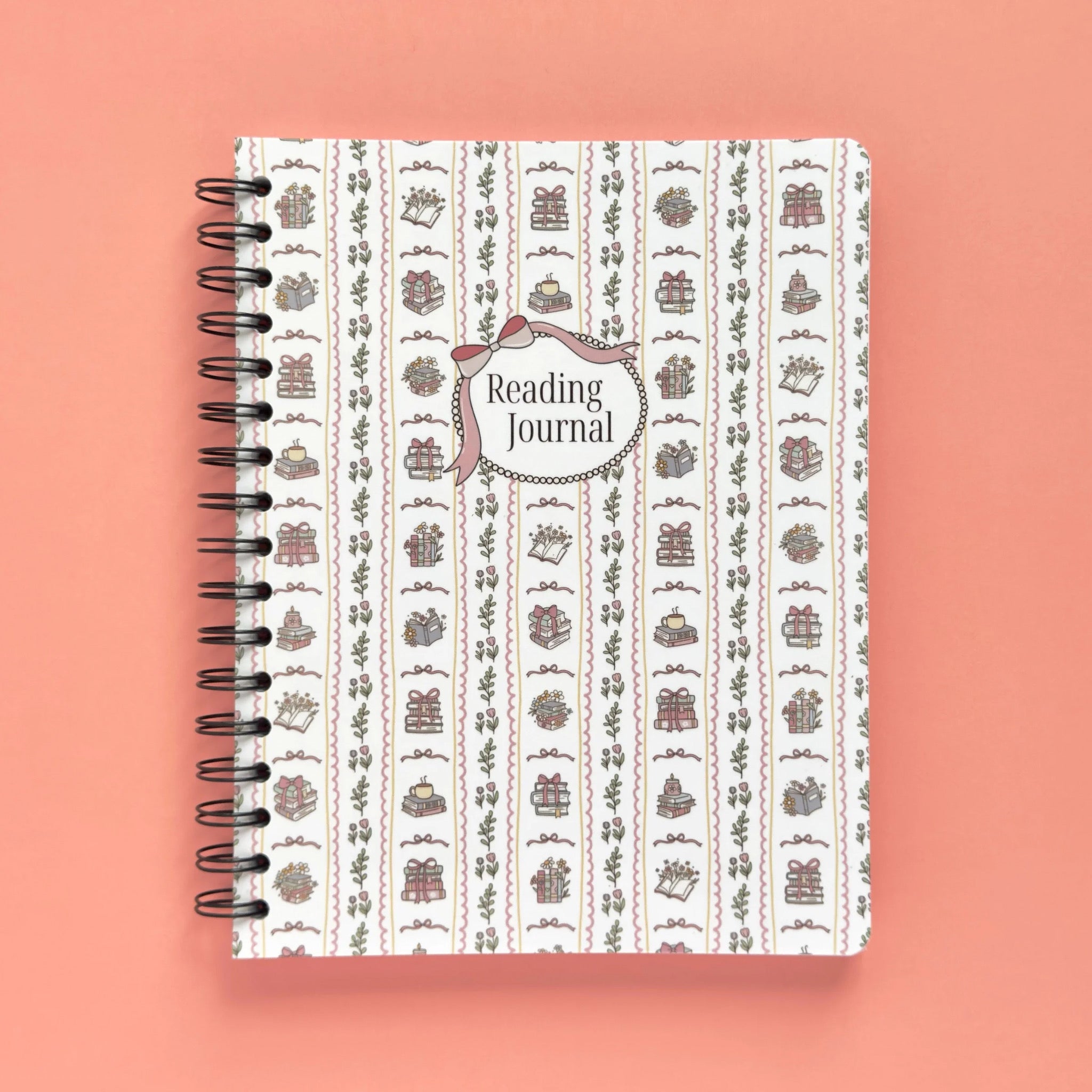 Spiral-bound softcover reading journal notebook with books and bows coquette cover design on a peach background