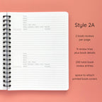 Open spiral-bound softcover reading journal notebook showing review template option Style 2A featuring two book reviews per page and nine review lines plus book details per review with space to attach printed book covers, displayed on a peach background