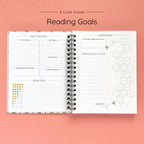 Open spiral-bound hardcover reading journal notebook showing reading goals and ratings guide on a peach background