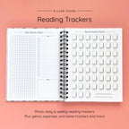 Open spiral-bound hardcover reading journal notebook showing daily and weekly reading trackers on a peach background