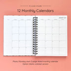 Open spiral-bound hardcover reading journal notebook showing monthly calendar pages on a peach background