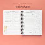 Open spiral-bound softcover reading journal notebook showing reading goals and ratings guide on a peach background