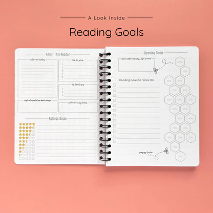 Open spiral-bound softcover reading journal notebook showing reading goals and ratings guide on a peach background
