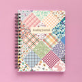 Spiral-bound softcover reading journal notebook with floral patchwork cover design on a lavender background