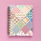 Spiral-bound softcover reading journal notebook with floral patchwork cover design on a lavender background