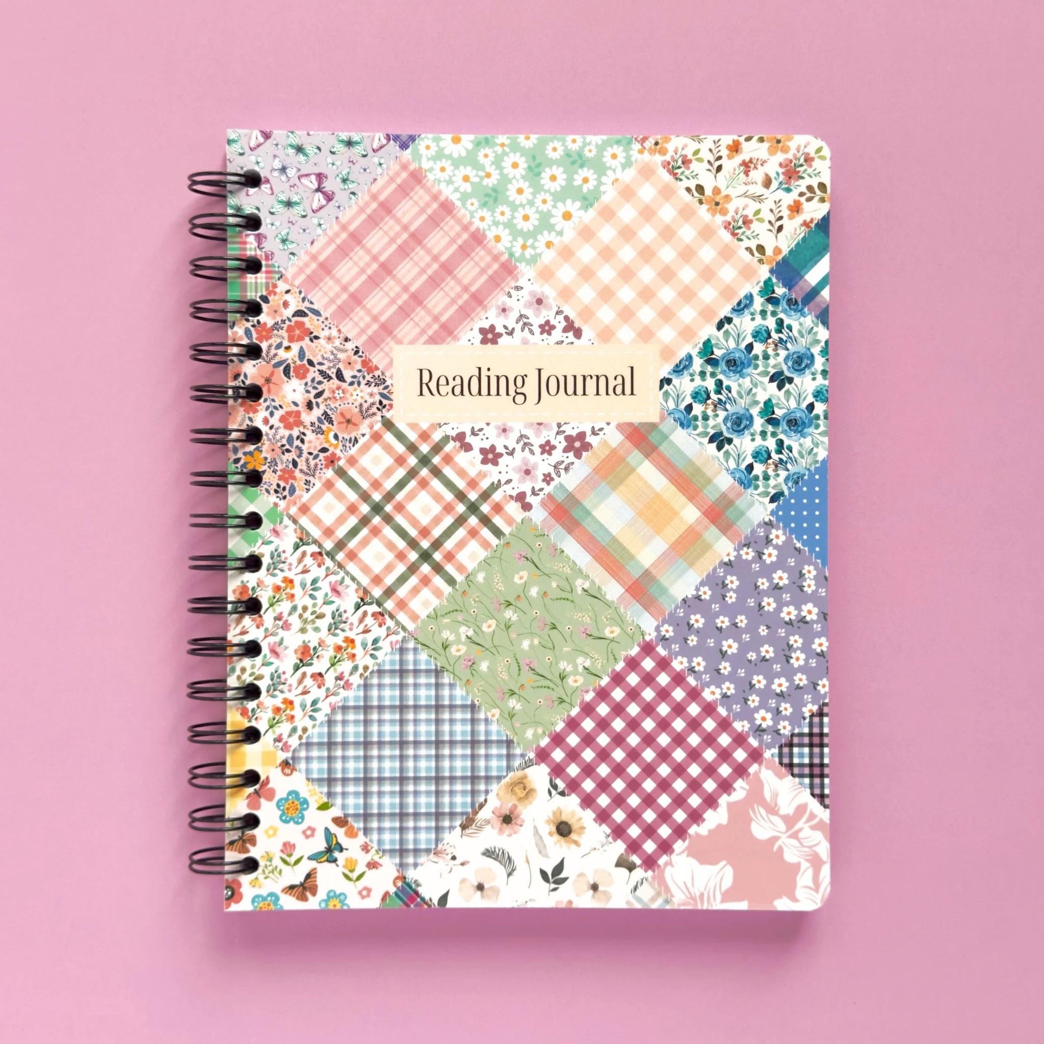 Spiral-bound softcover reading journal notebook with floral patchwork cover design on a lavender background