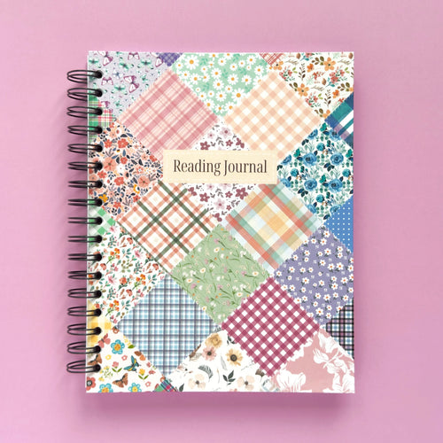 Spiral-bound hardcover reading journal notebook with floral patchwork cover design on a lavender background