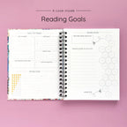 Open spiral-bound hardcover reading journal notebook showing reading goals and ratings guide on a lavender background