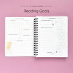 Open spiral-bound softcover reading journal notebook showing reading goals and ratings guide on a lavender background