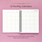 Open spiral-bound softcover reading journal notebook showing monthly calendar pages on a lavender background