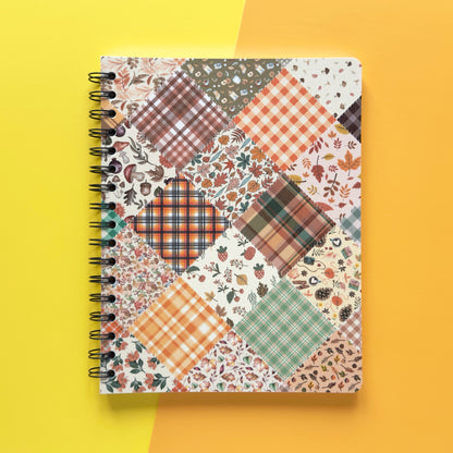 Spiral-bound softcover lined notebook with autumn patchwork cover design on a yellow and orange background, featuring black wire binding