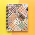 Spiral-bound hardcover lined notebook with autumn patchwork cover design on a yellow and orange background
