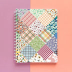 Spiral-bound softcover lined notebook with floral patchwork cover design on a lavender and peach background, featuring white wire binding
