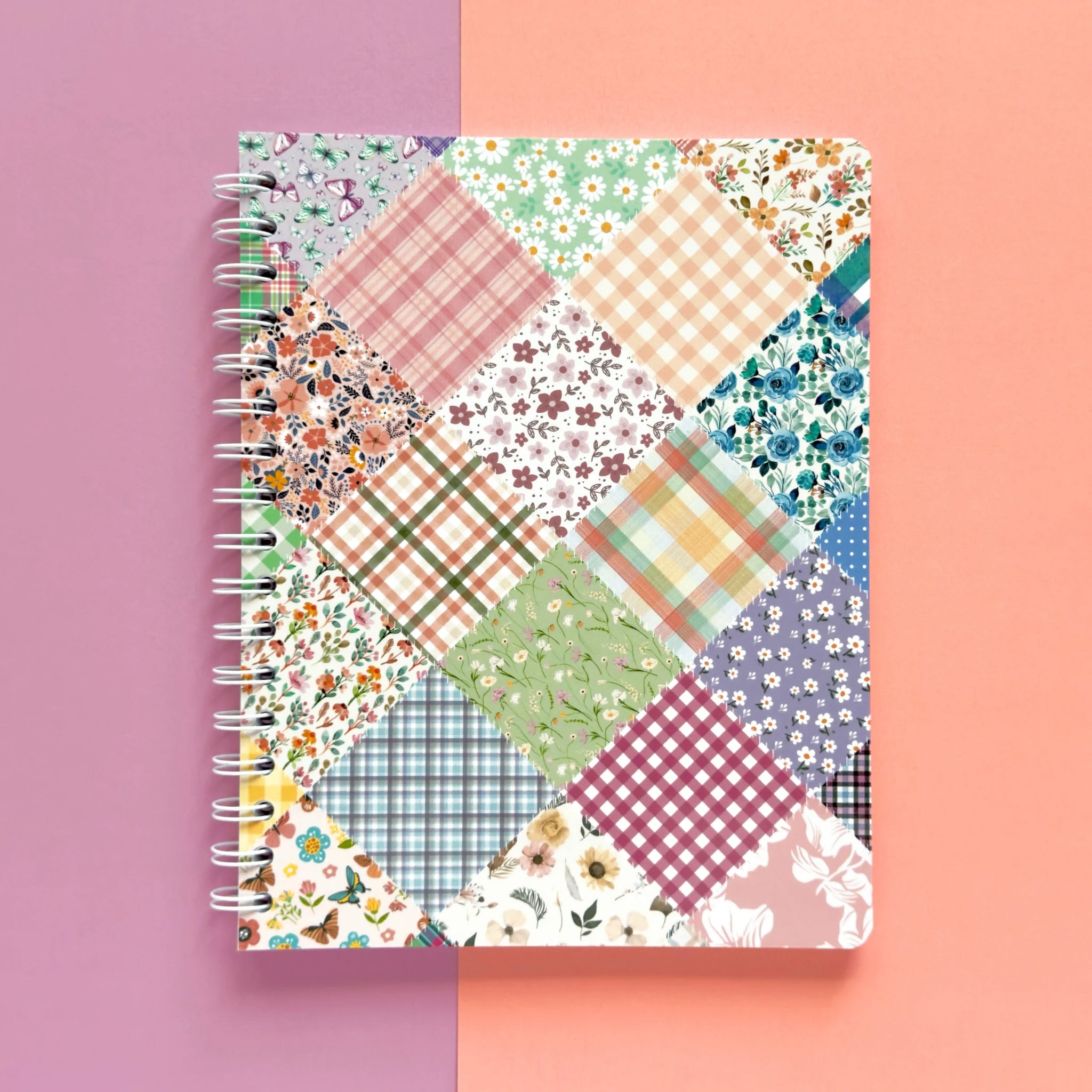 Spiral-bound softcover lined notebook with floral patchwork cover design on a lavender and peach background, featuring white wire binding