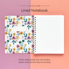 Open spiral-bound softcover lined notebook showing lined notes pages on a lavender and peach background, featuring white wire binding