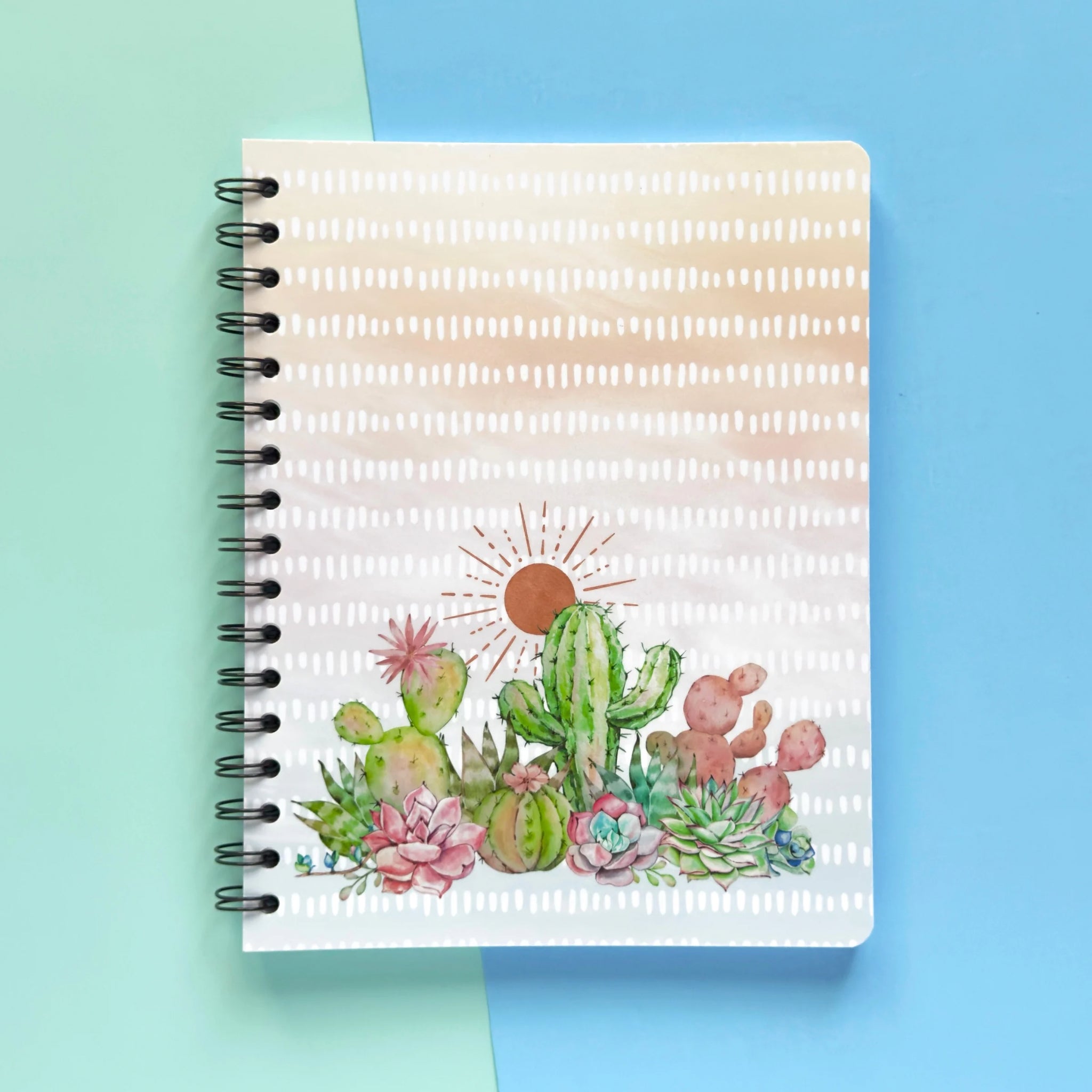 Spiral-bound softcover lined notebook with cactus and succulent cover design on a teal and blue background, featuring black double loop wire binding
