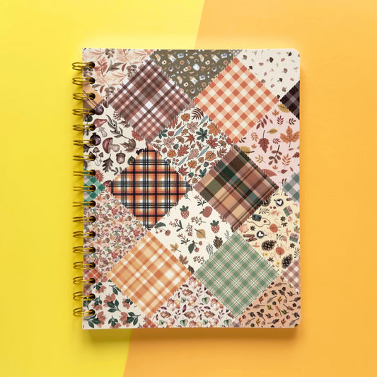 Spiral-bound softcover lined notebook with autumn patchwork cover design on a yellow and orange background, featuring gold wire binding