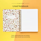 Open spiral-bound softcover lined notebook showing lined notes pages on a yellow and orange background, featuring gold wire binding