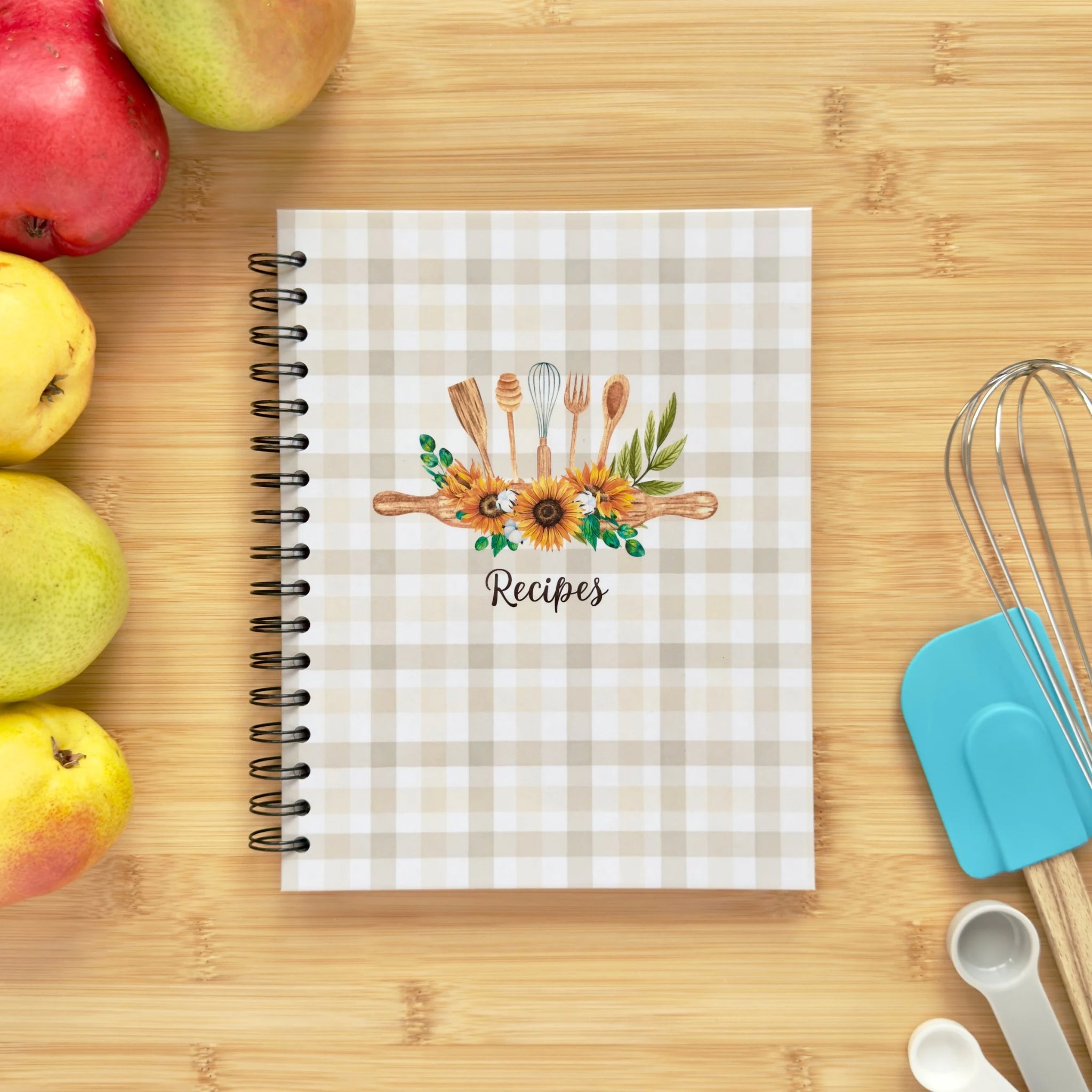 Spiral-bound hardcover recipe book notebook with kitchen tools and sunflowers cover design on a wooden surface with kitchen utensils and pears